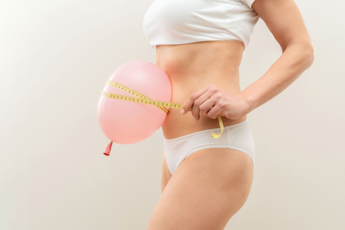 femeie tine un balon roz pe abdomen cu un metru de croitorie